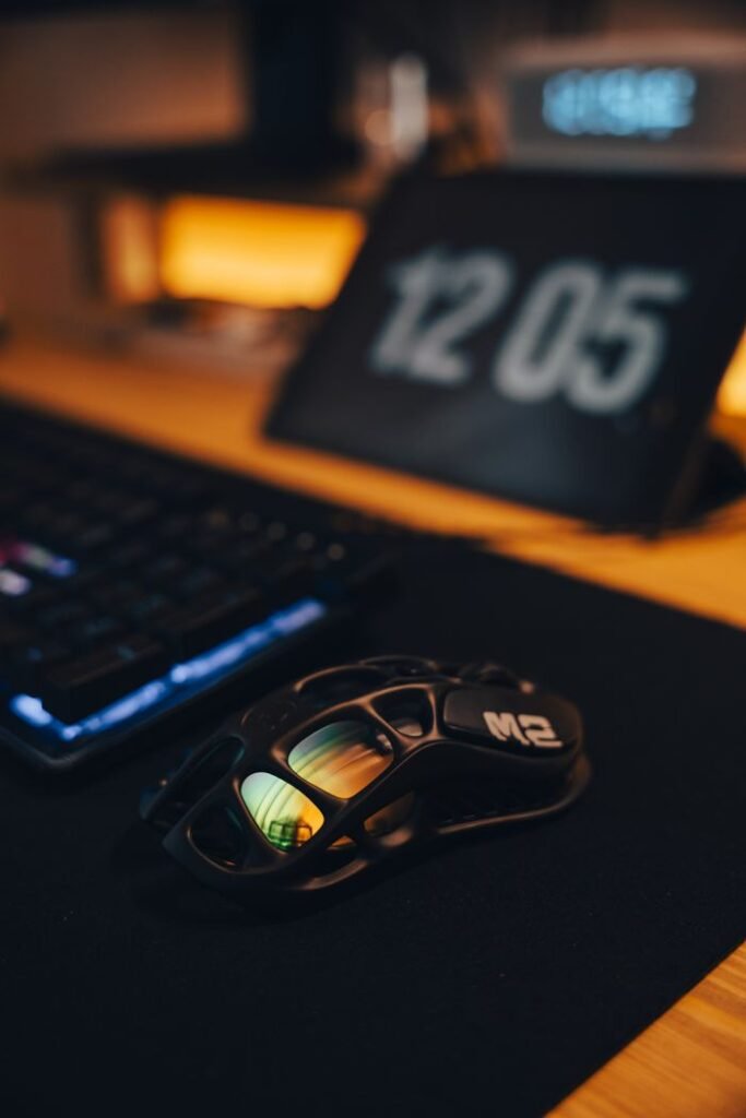 A sleek gaming desk setup featuring a futuristic mouse, keyboard, and digital clock with ambient RGB lighting.